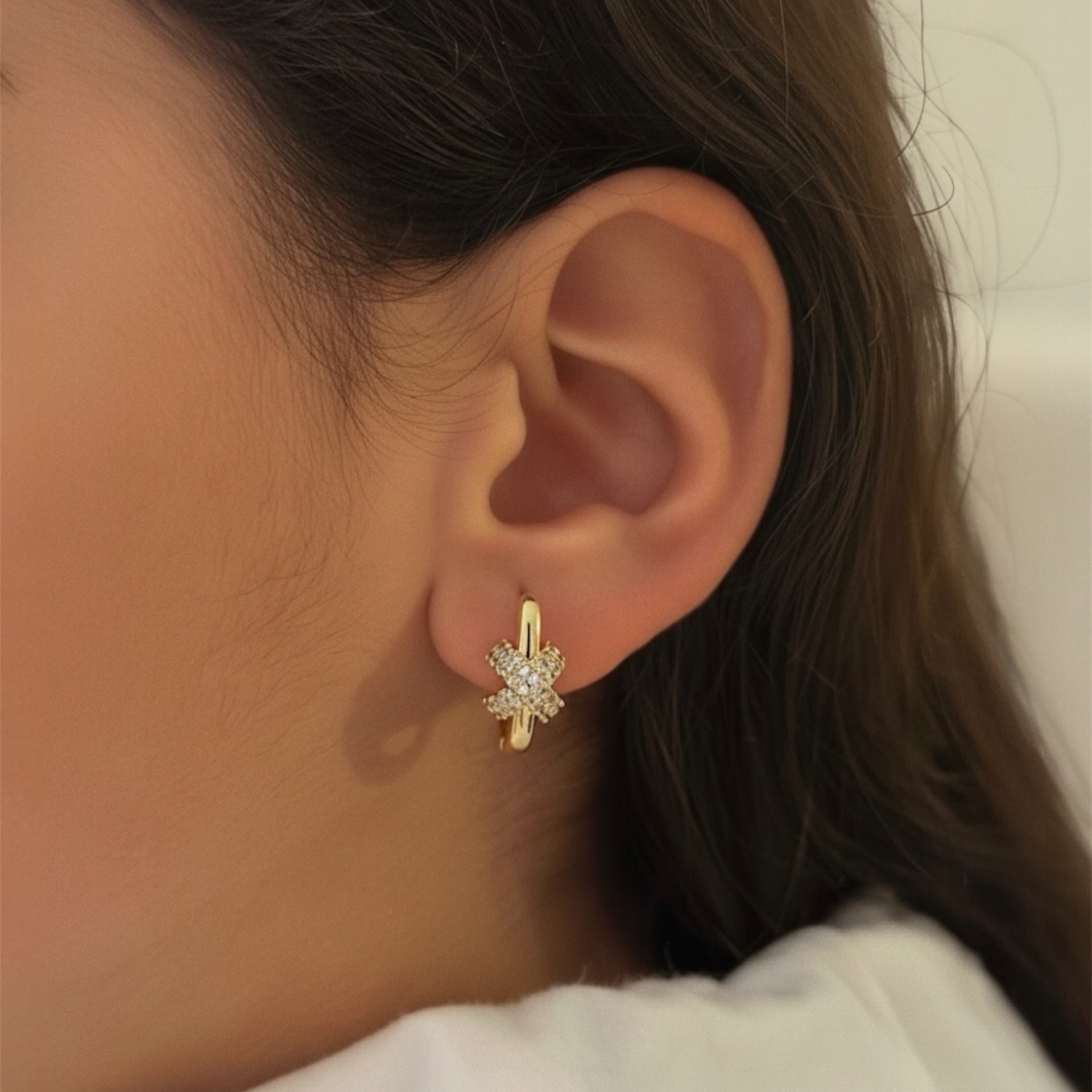 Close-up of a person wearing a gold earring with a diamond-like stone.