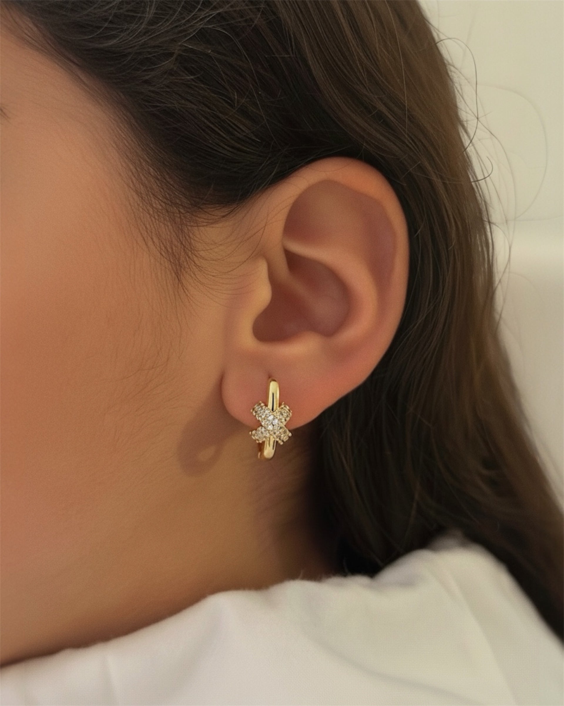 Close-up of a person wearing a gold earring with a diamond-like stone.