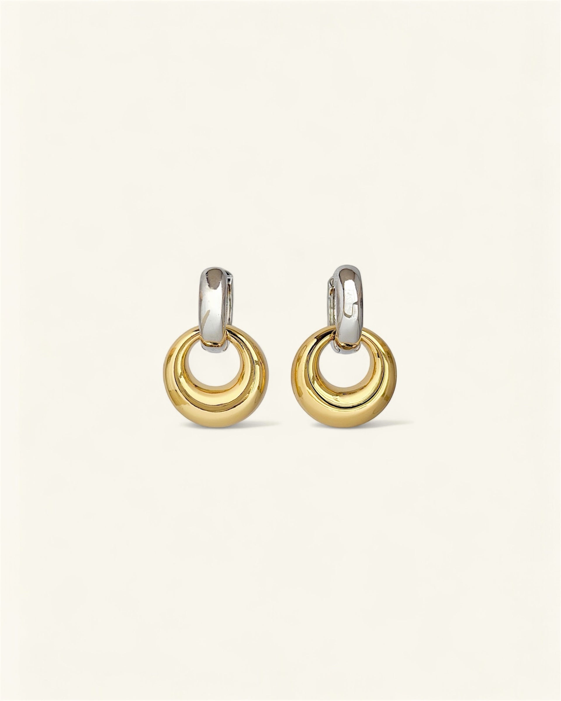 Pair of gold and silver hoop earrings on a light beige background