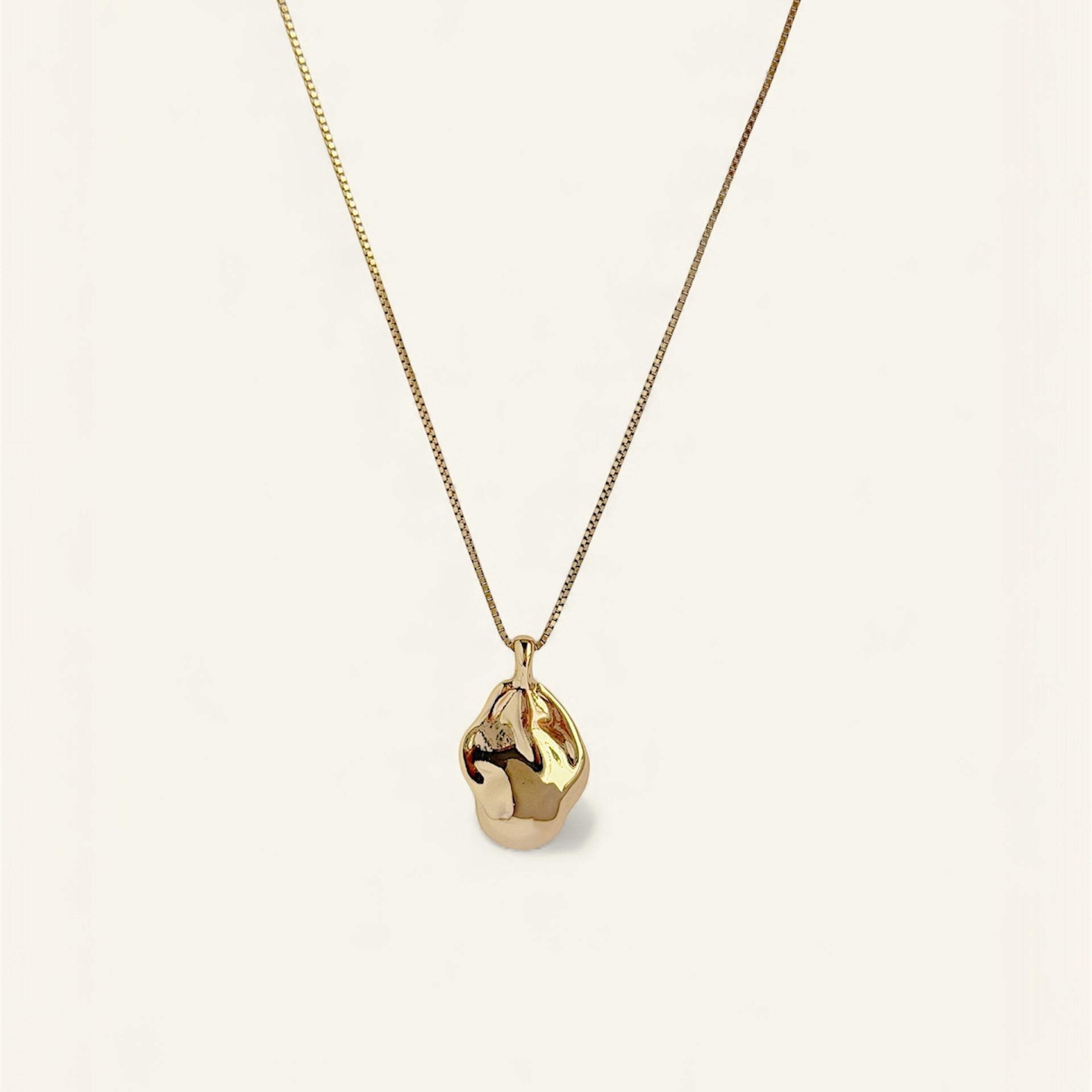 Gold necklace with a teardrop-shaped pendant on a light beige background