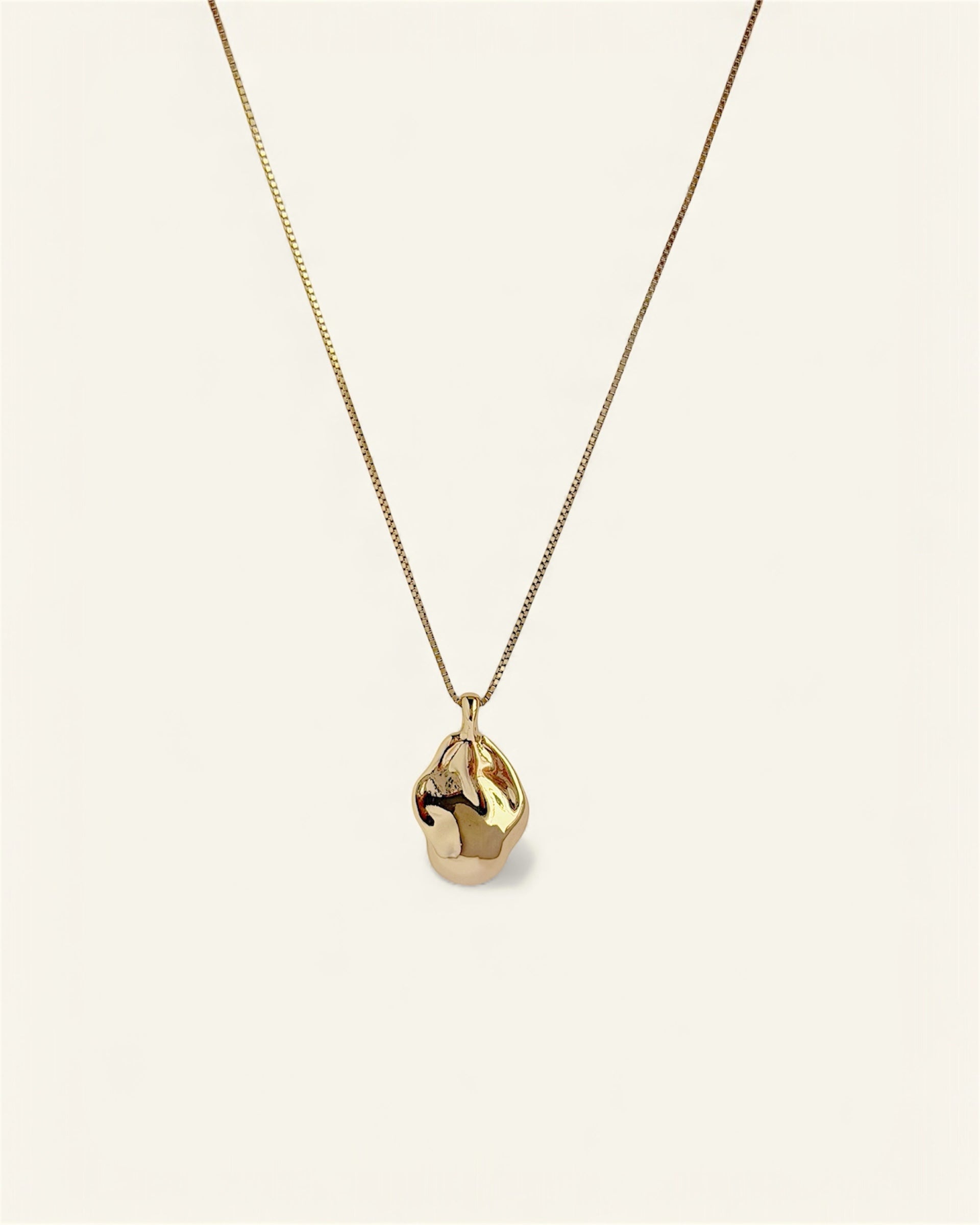 Gold necklace with a teardrop-shaped pendant on a light beige background