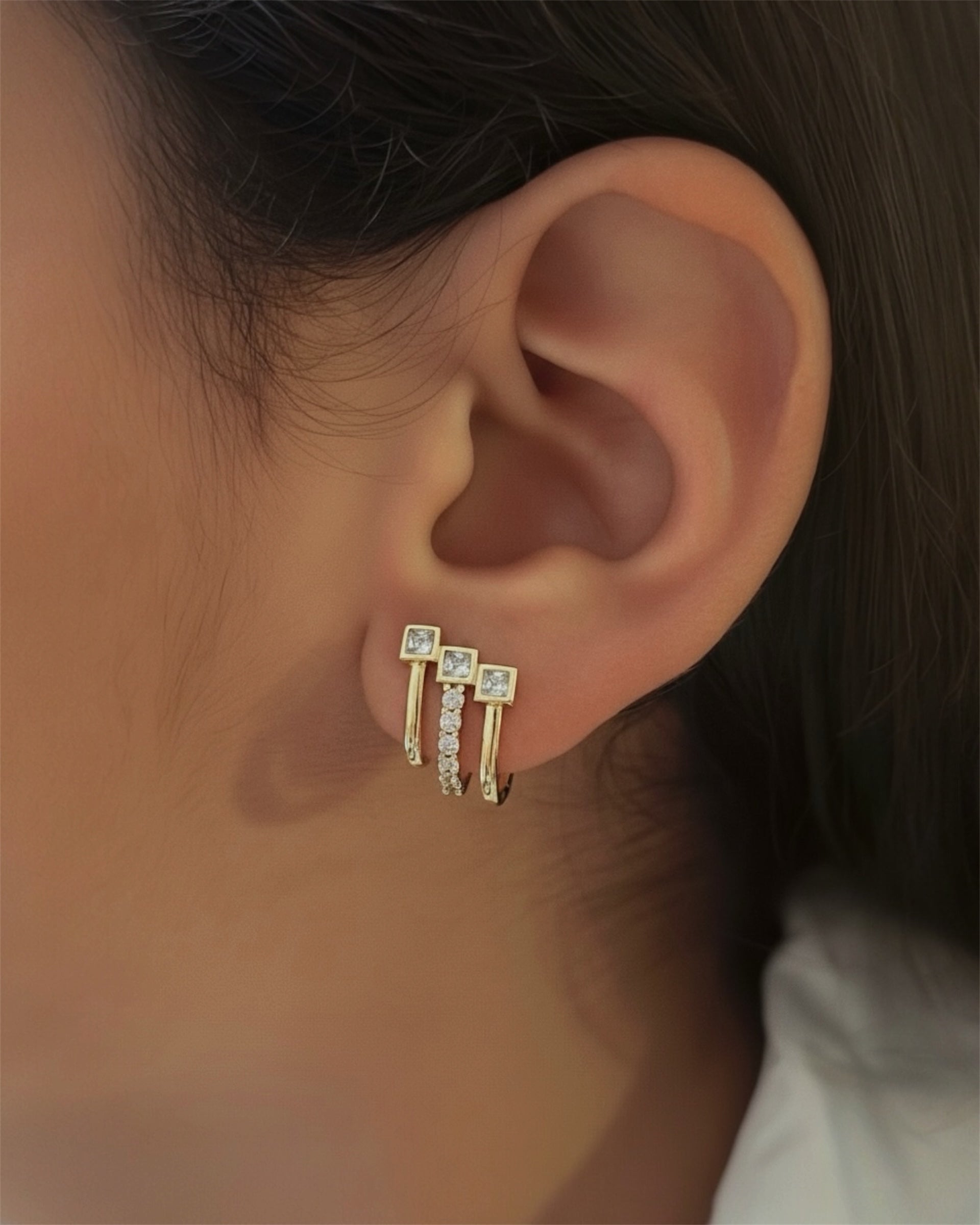 Close-up of an ear wearing a set of gold earrings with clear stones.