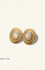 Pair of gold earrings with pearl-like centers on a light beige background