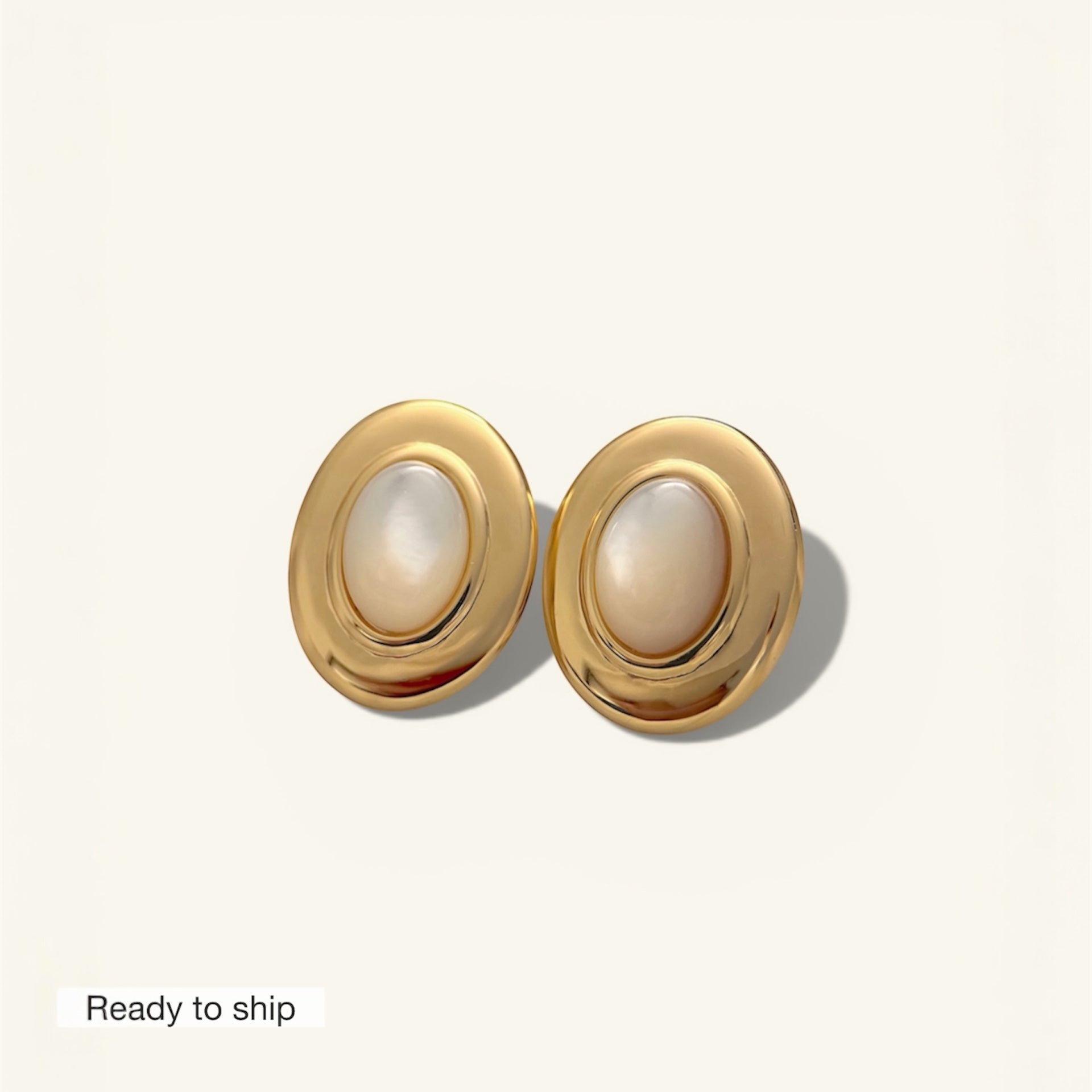 Pair of gold earrings with pearl-like centers on a light beige background