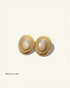 Pair of gold earrings with pearl-like centers on a light beige background