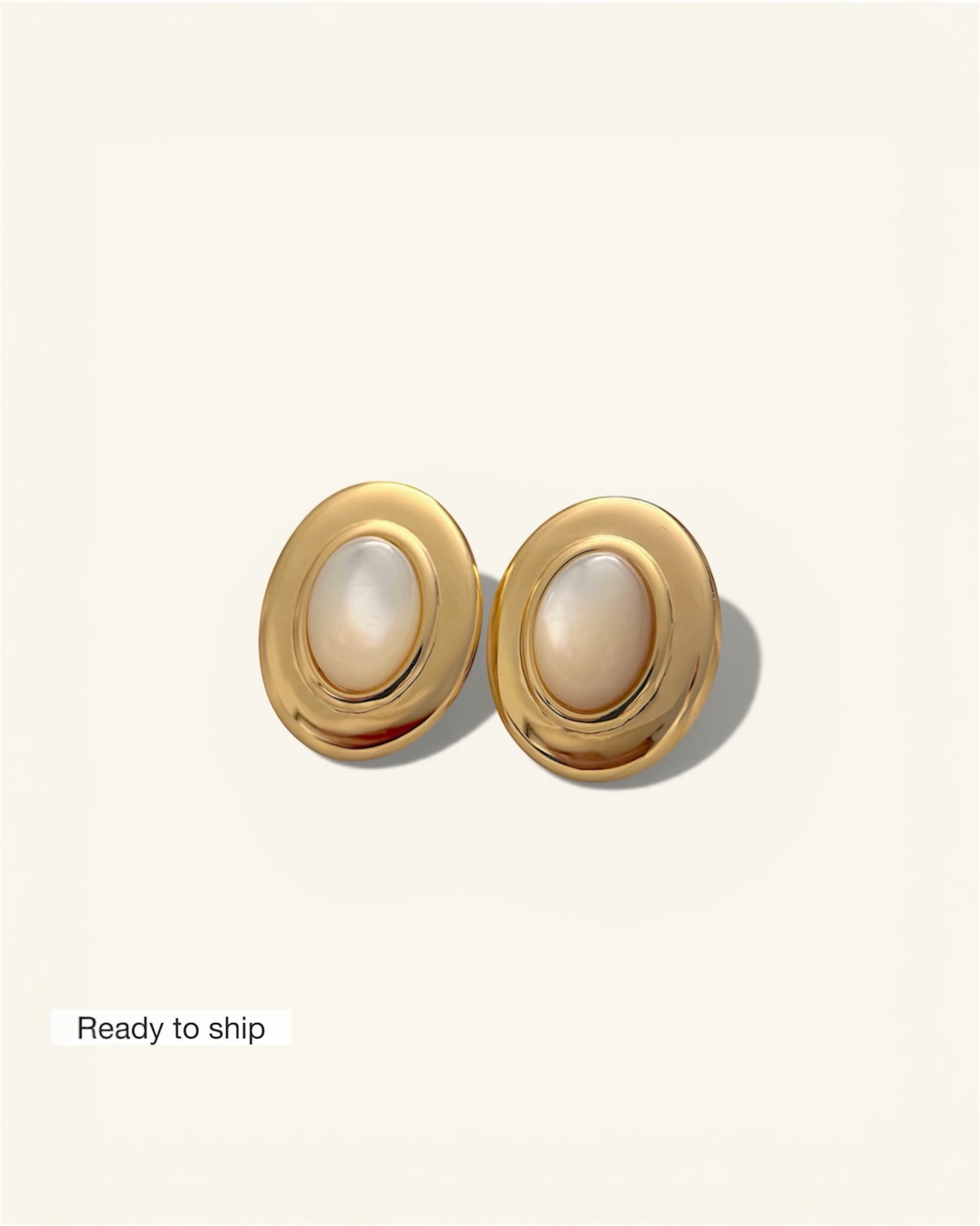 Pair of gold earrings with pearl-like centers on a light beige background
